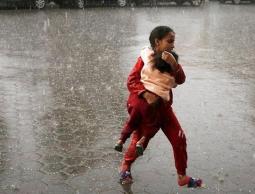 طفلة من غزة تحمي شقيقها من المطر في أحد مراكز النزوح.jpg